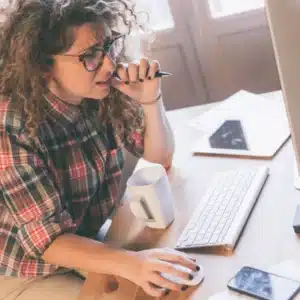 Office worker troubleshoots computer issues at desk, coffee in hand; IT services for small business