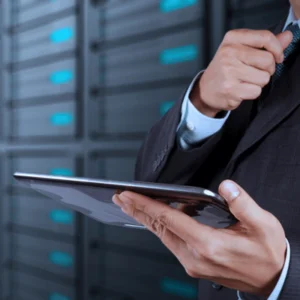 Business professional reviews server metrics on tablet in data hall; photo emphasizes compliance oversight responsibilities