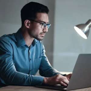 Analyst works late at laptop, applying hardening standards checklists to configure systems securely at scale
