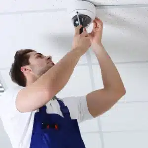 Professional security camera installers setting up a dome surveillance camera on an office ceiling using tools