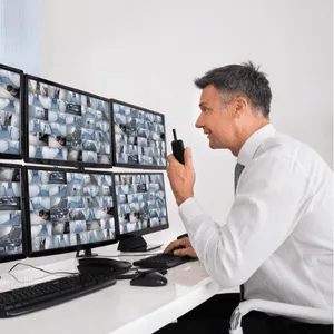 Security officer monitors multiple security camera feeds on large screens using a walkie-talkie system