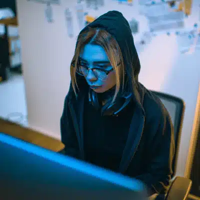 Hooded cybersecurity specialist works at desktop computer, defending companies through advanced it support services tonight