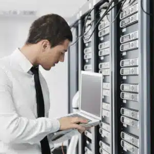 Engineer evaluates server racks using laptop, verifying connections, performance metrics, and troubleshooting network issues today