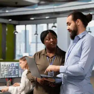 Engineers discuss network refresh strategy on office floor, reviewing laptop dashboards and deployment timelines together