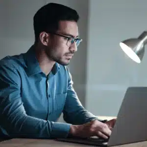 Analyst works late at laptop, applying hardening standards checklists to configure systems securely at scale