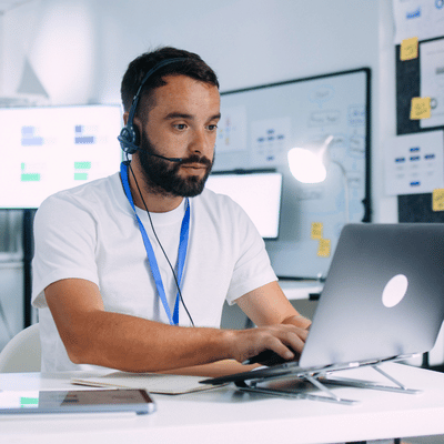 A headset support agent works on a laptop, delivering IT services for small business troubleshooting