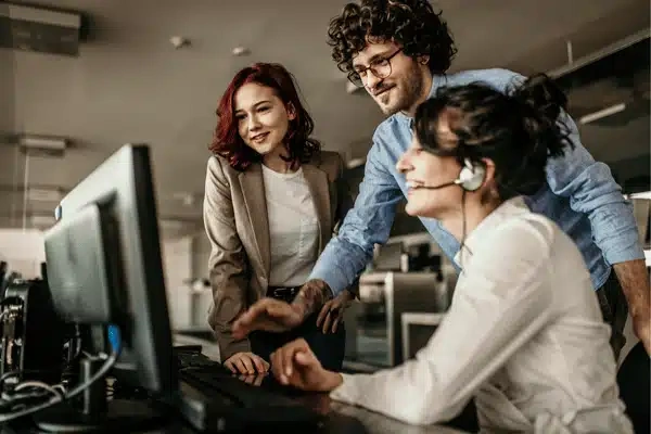 Photo shows team guiding headset agent at computer, representing it support company helpdesk collaboration today