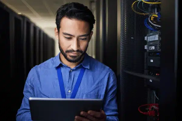 Technician checks tablet beside server racks, representing proactive it support services monitoring business networks today