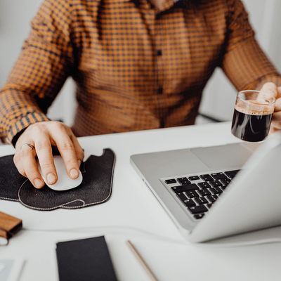A worker uses a mouse beside a laptop and coffee, relying on IT services for small business
